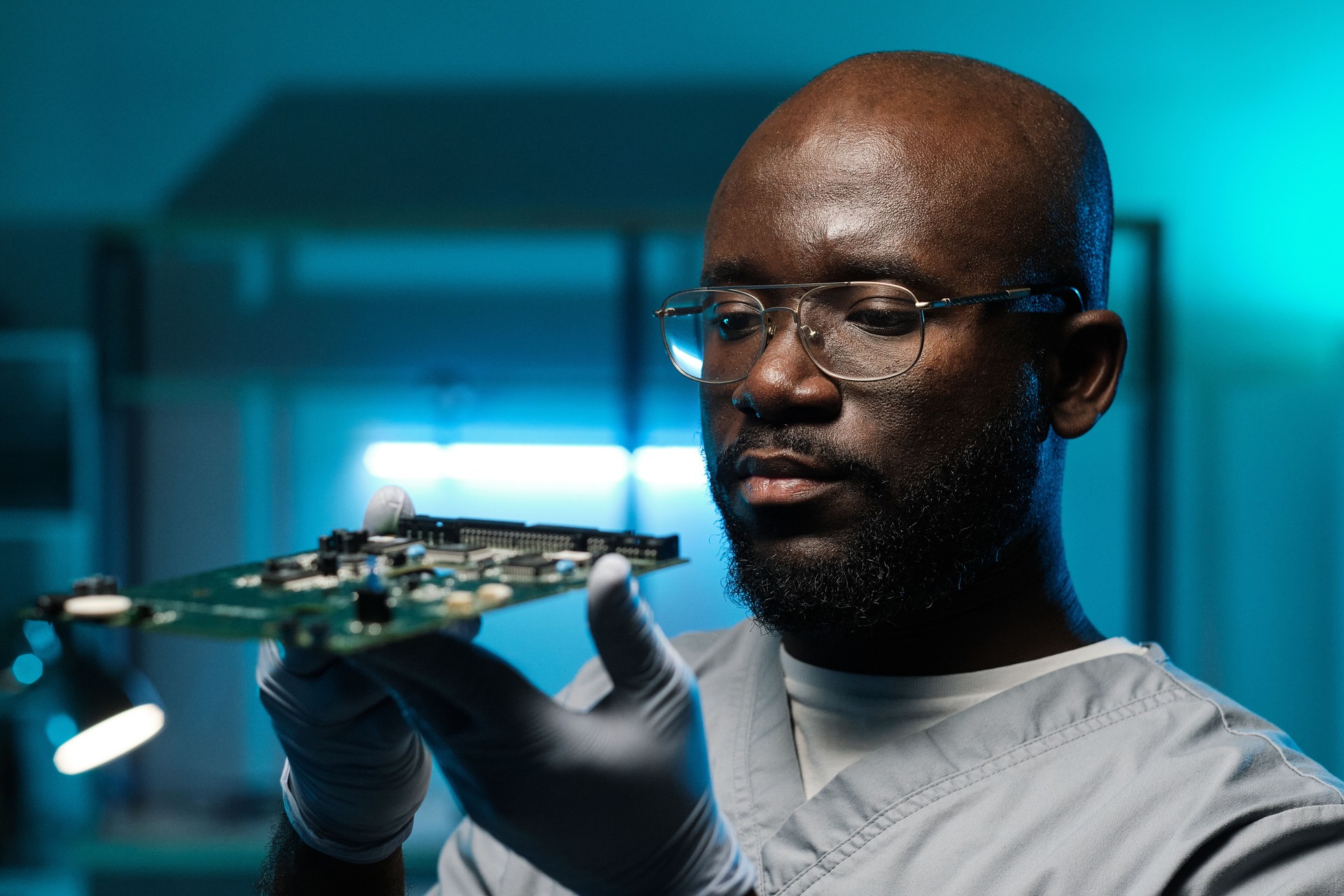 Serious African repairman in gloves and uniform holding circuit board