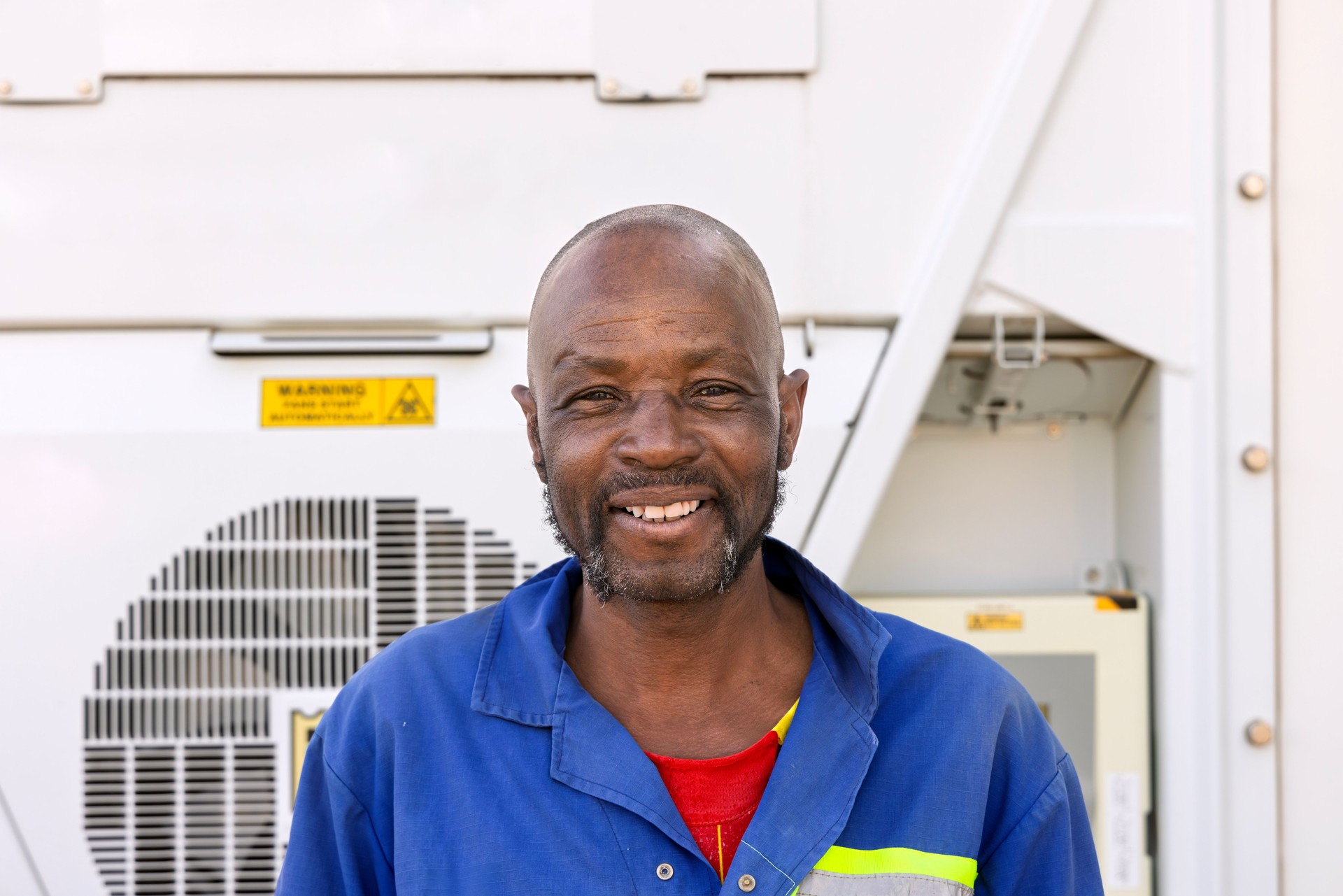 workers African at ac HVAC air conditioner container refrigeration units containers portable, repair technician wearing workwear high visibility safety with reflective yellow